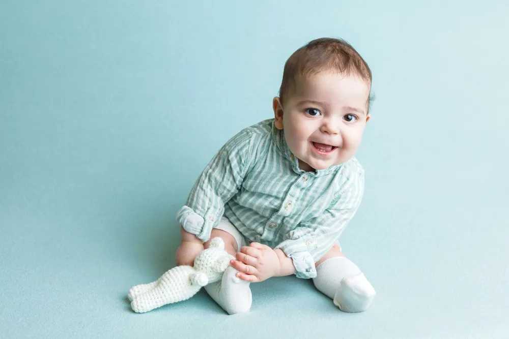 Bebé sorridente sentado num fundo azul, de camisa às riscas