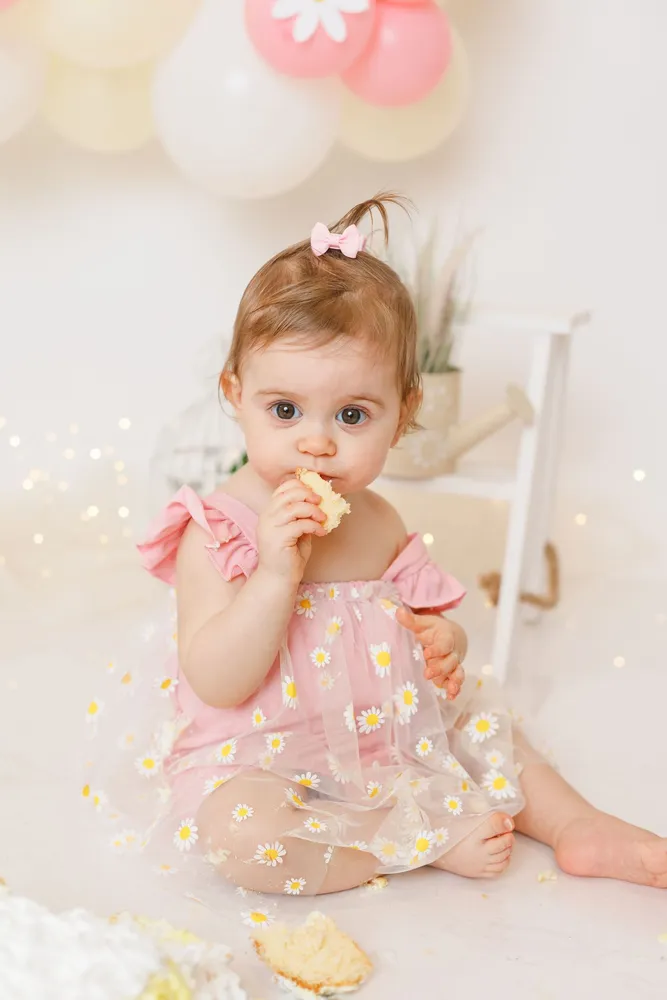 Bebé de vestido cor-de-rosa a provar o bolo numa sessão smash the cake