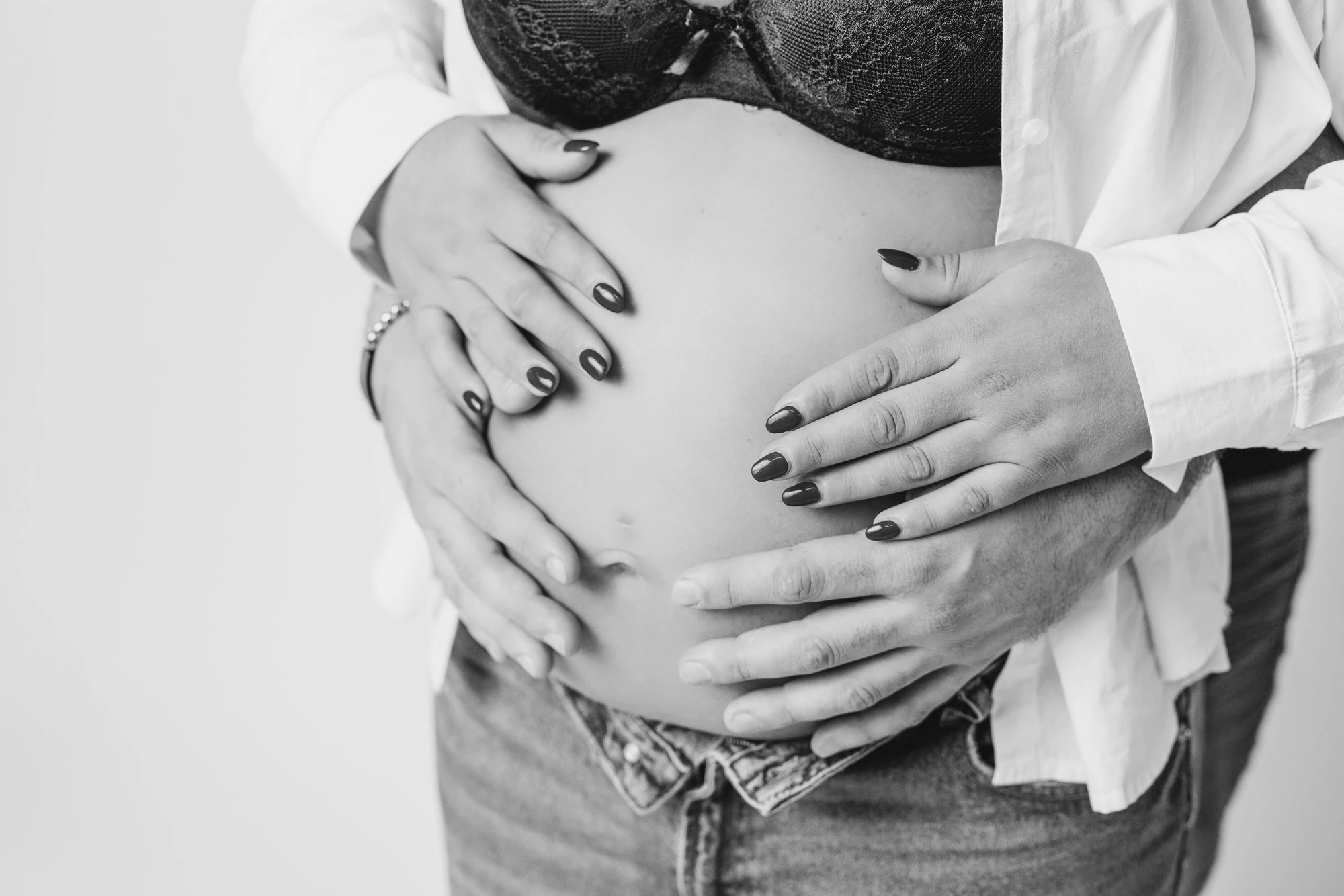 Mãos da mãe e do pai sobre a barriga da grávida, a preto e branco