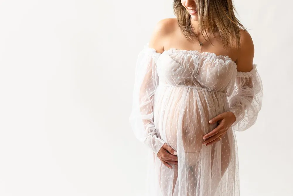 Grávida de vestido de renda branca transparente, com as mãos sob a barriga