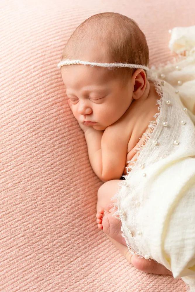 Recém-nascida a dormir encolhida, num fundo rosa