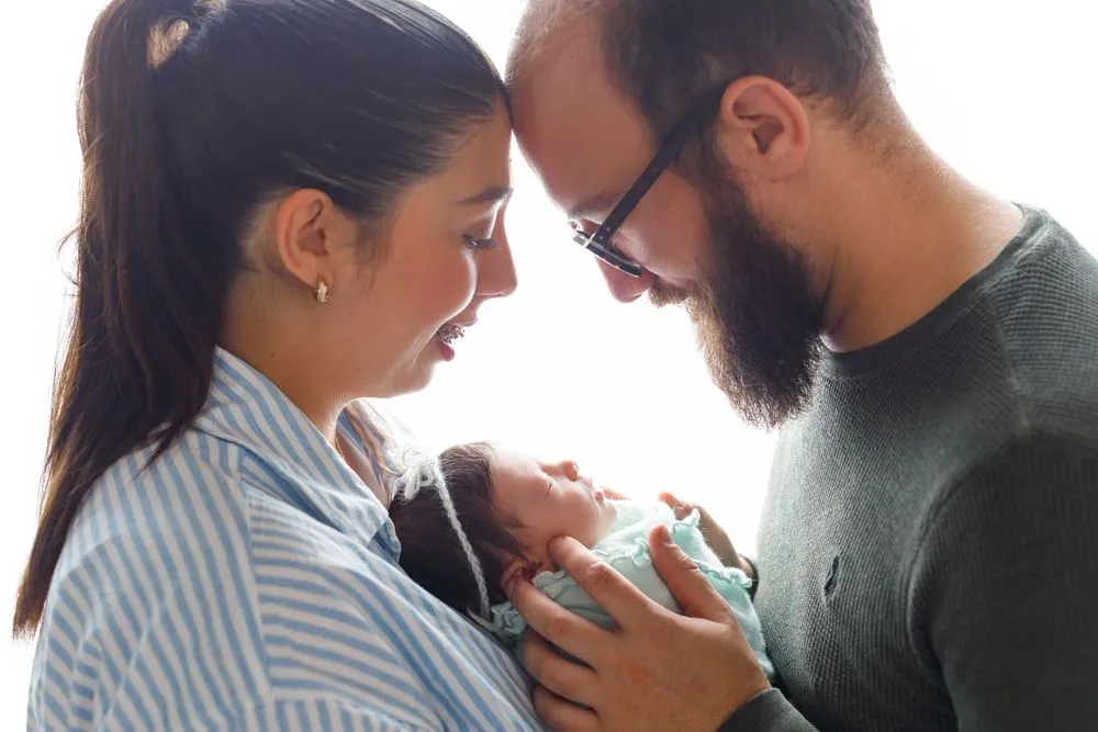 Mãe e pai encostam as testas, com o bebé recém-nascido ao colo